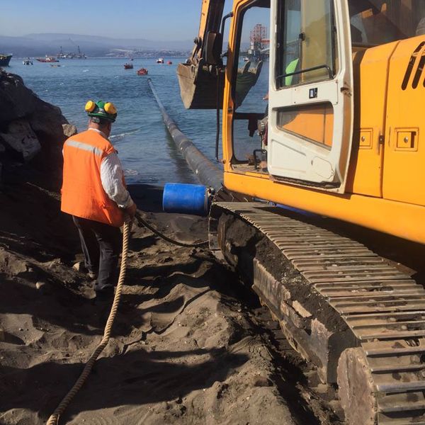 Excavadora y trabajador instalando una tubería en la playa