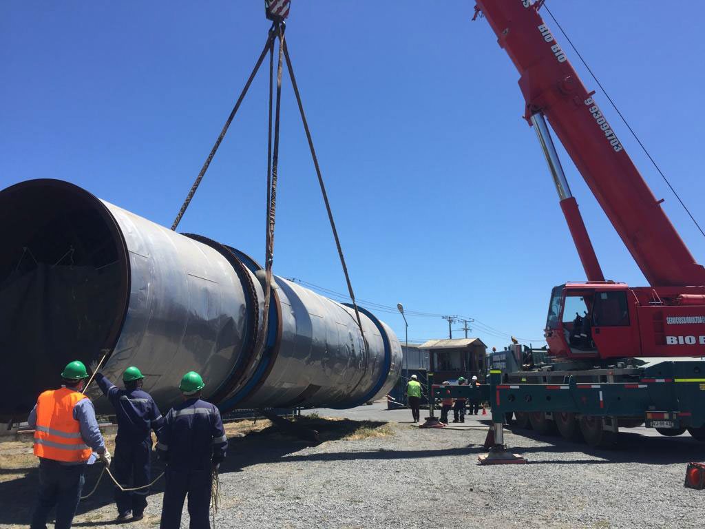 Grúa izando un tambor industrial de gran diámetro con una cuadrilla en terreno